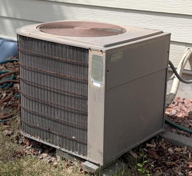 A weathered Lennox air conditioning unit sits beside a house, partially surrounded by landscaping.