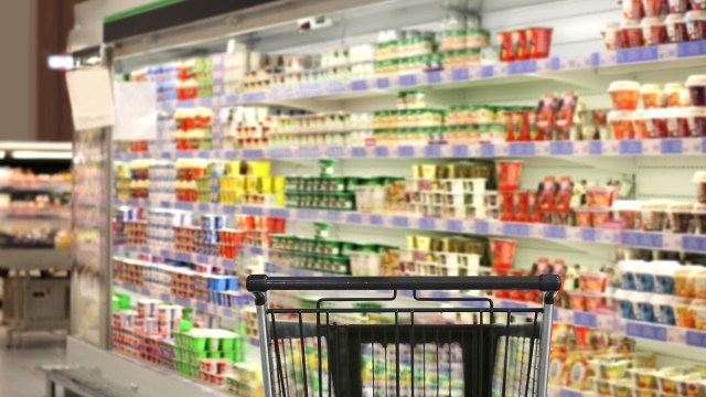A shopping cart in front of colorful shelves filled with various dairy products in a supermarket.