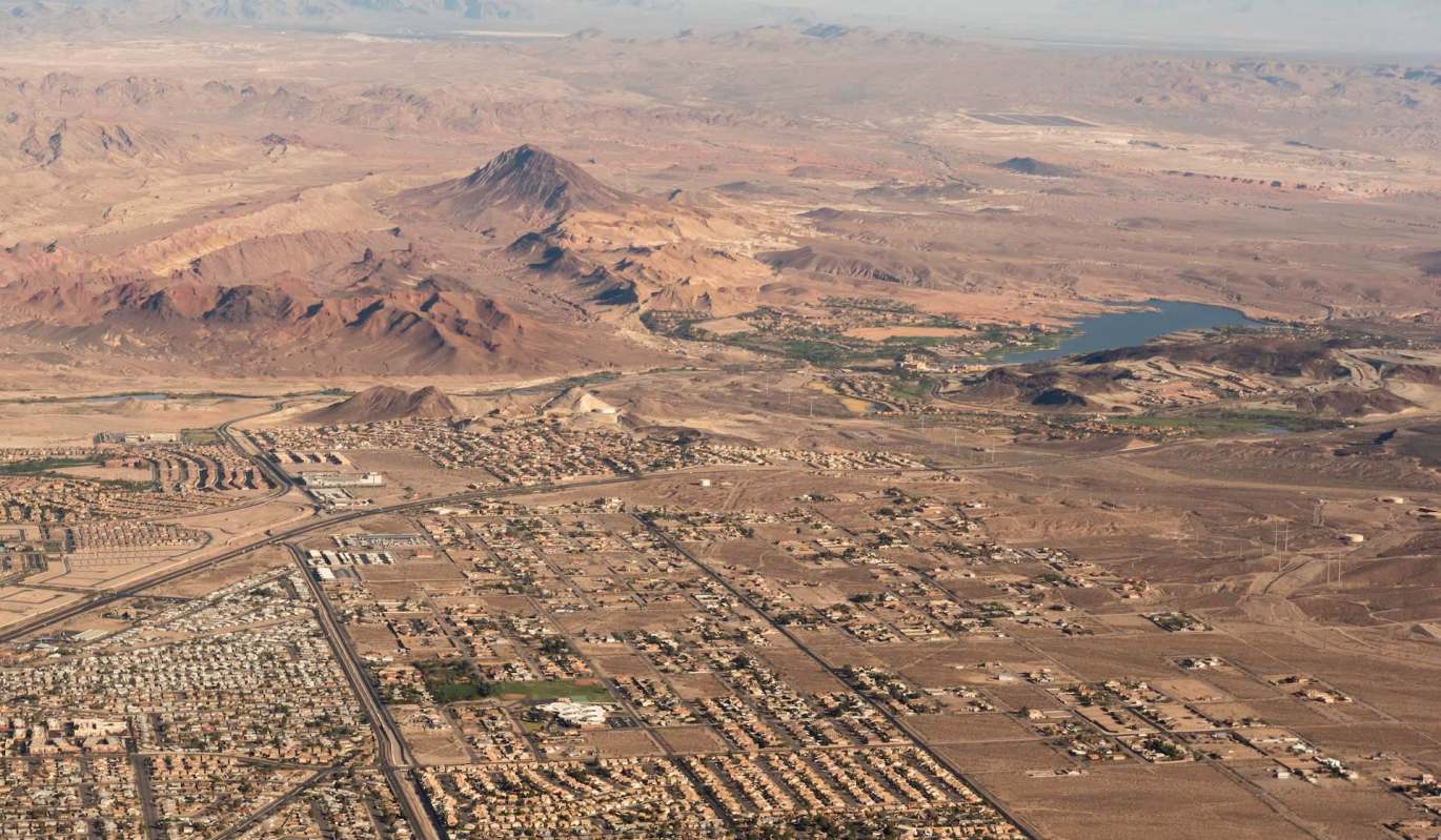 An aerial view of a desert landscape featuring mountains, a lake, and sprawling urban development.