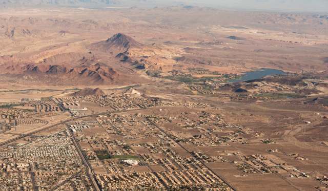 An aerial view of a desert landscape featuring mountains, a lake, and sprawling urban development.