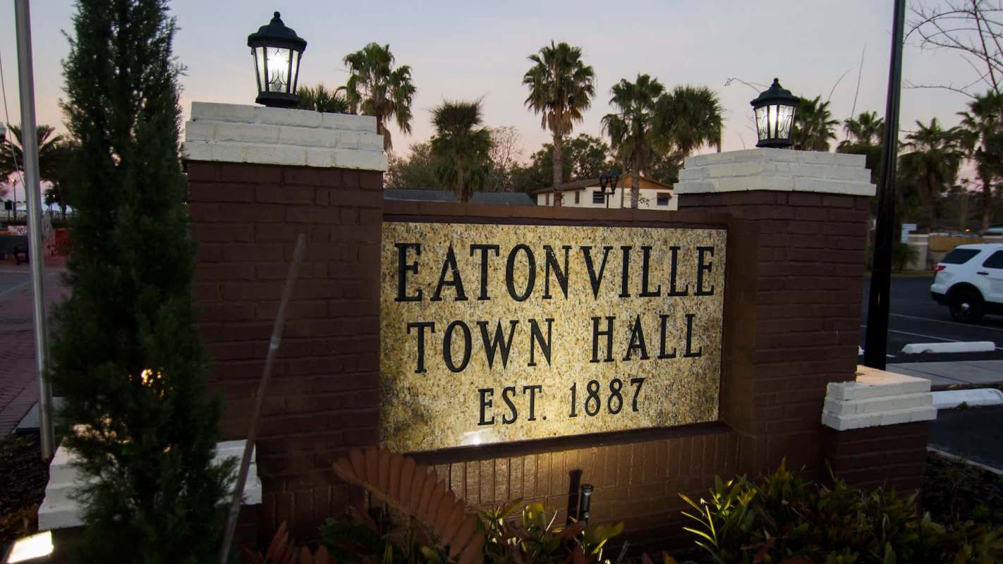 A sign for Eatonville Town Hall, established in 1887, outlined by palm trees and decorative lighting.