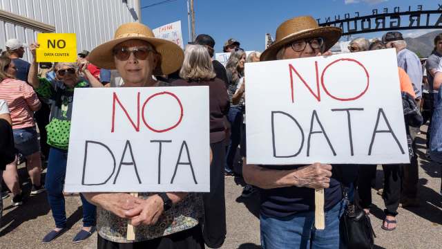 Two elderly women hold large signs reading "NO DATA" while participating in a protest in a crowded outdoor setting.