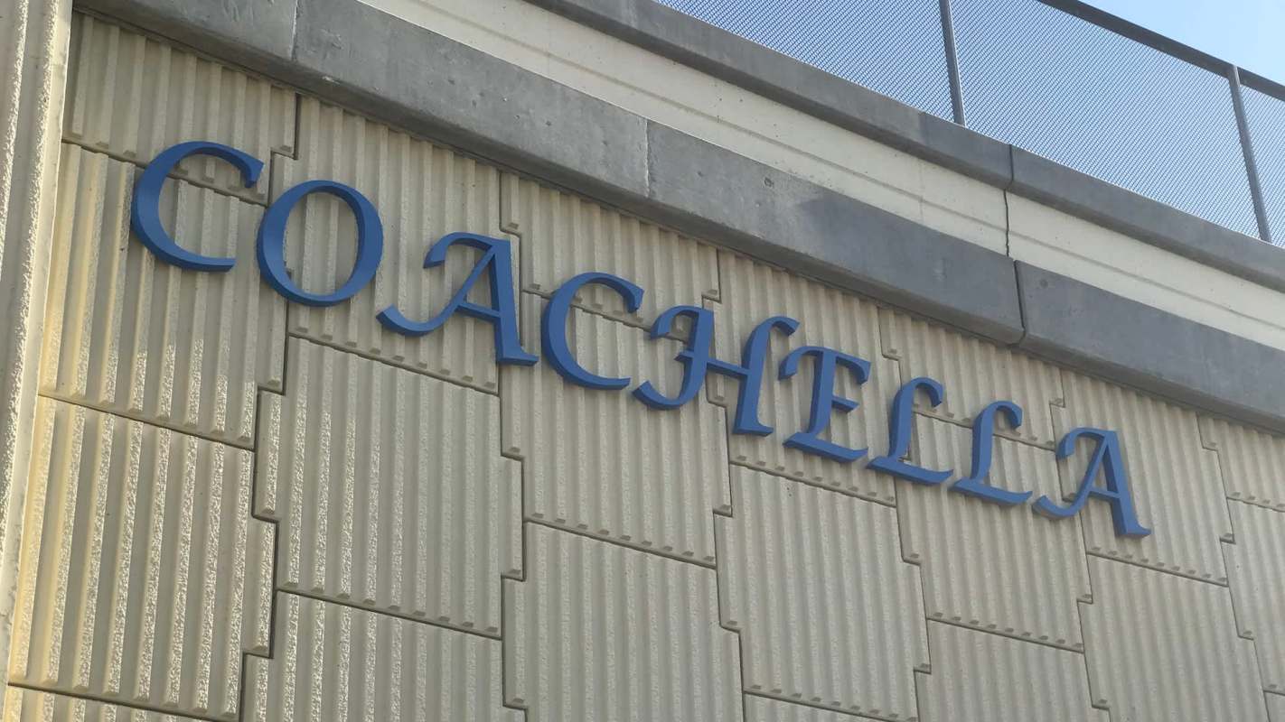 A blue "Coachella" sign mounted on a textured beige wall.