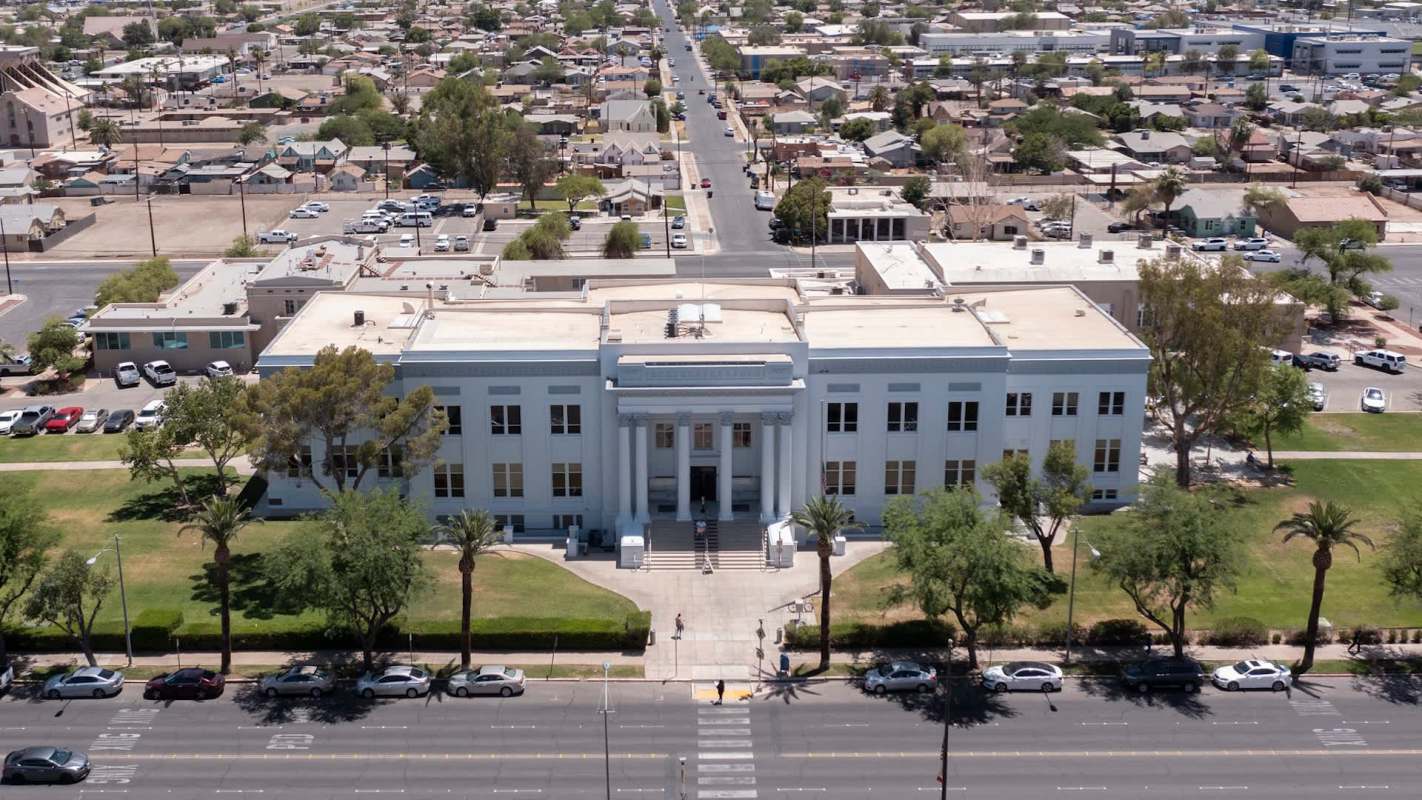 Aerial view of a large, white government building surrounded by green lawns and a cityscape in the background.