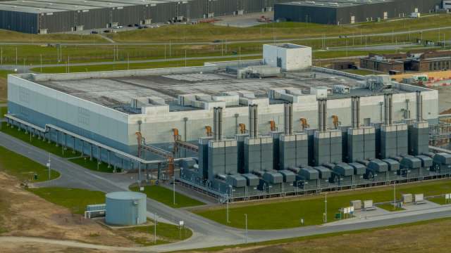 An aerial view of an industrial facility with cooling towers and large gray buildings surrounded by greenery.
