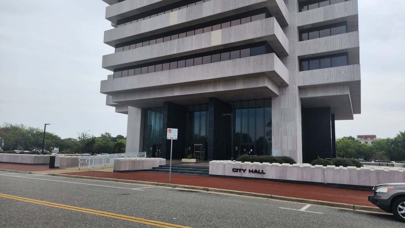 A modern city hall building with a distinctive façade and large glass entrance, surrounded by greenery.