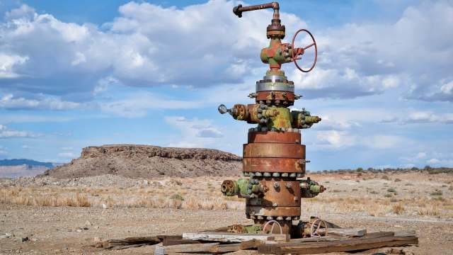 An old oil wellhead stands in a dry, desert landscape under a partly cloudy sky.