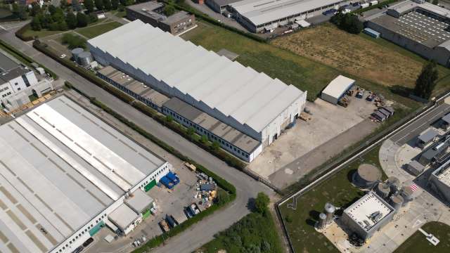 An aerial view of industrial buildings and storage areas surrounded by greenery and roads.