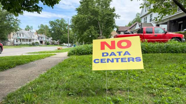 A bright yellow sign says "NO DATA CENTERS" in bold letters, placed on a grassy sidewalk in a neighborhood.