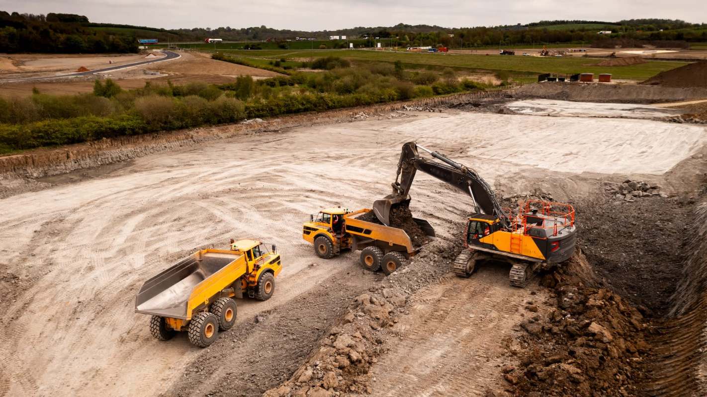 Two yellow dump trucks and an excavator working at a construction site.