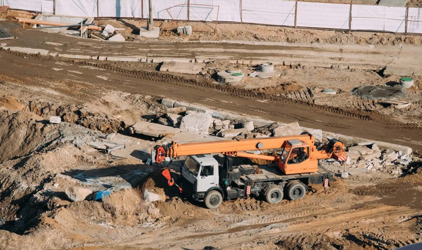 A construction site featuring a crane on uneven ground with scattered debris and unfinished pathways.