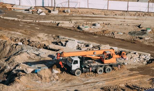 A construction site featuring a crane on uneven ground with scattered debris and unfinished pathways.