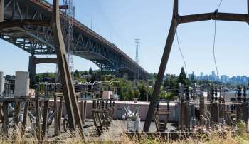 A view of a large bridge spanning over industrial infrastructure with a city skyline in the background.