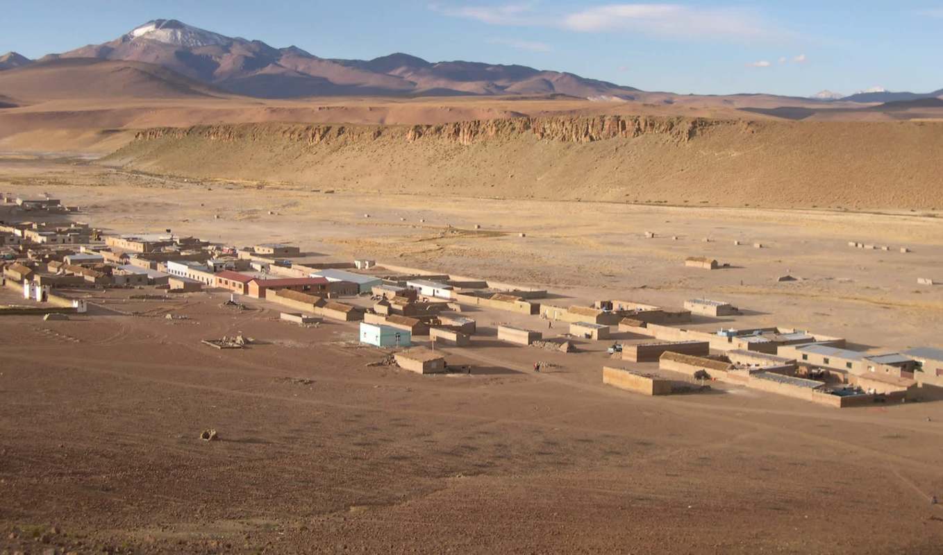 A remote settlement with mud houses set against a backdrop of mountains and arid, empty landscapes.