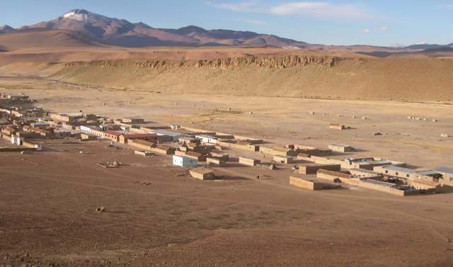 A remote settlement with mud houses set against a backdrop of mountains and arid, empty landscapes.