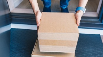 A person picks up a cardboard box stacked on top of a second box.