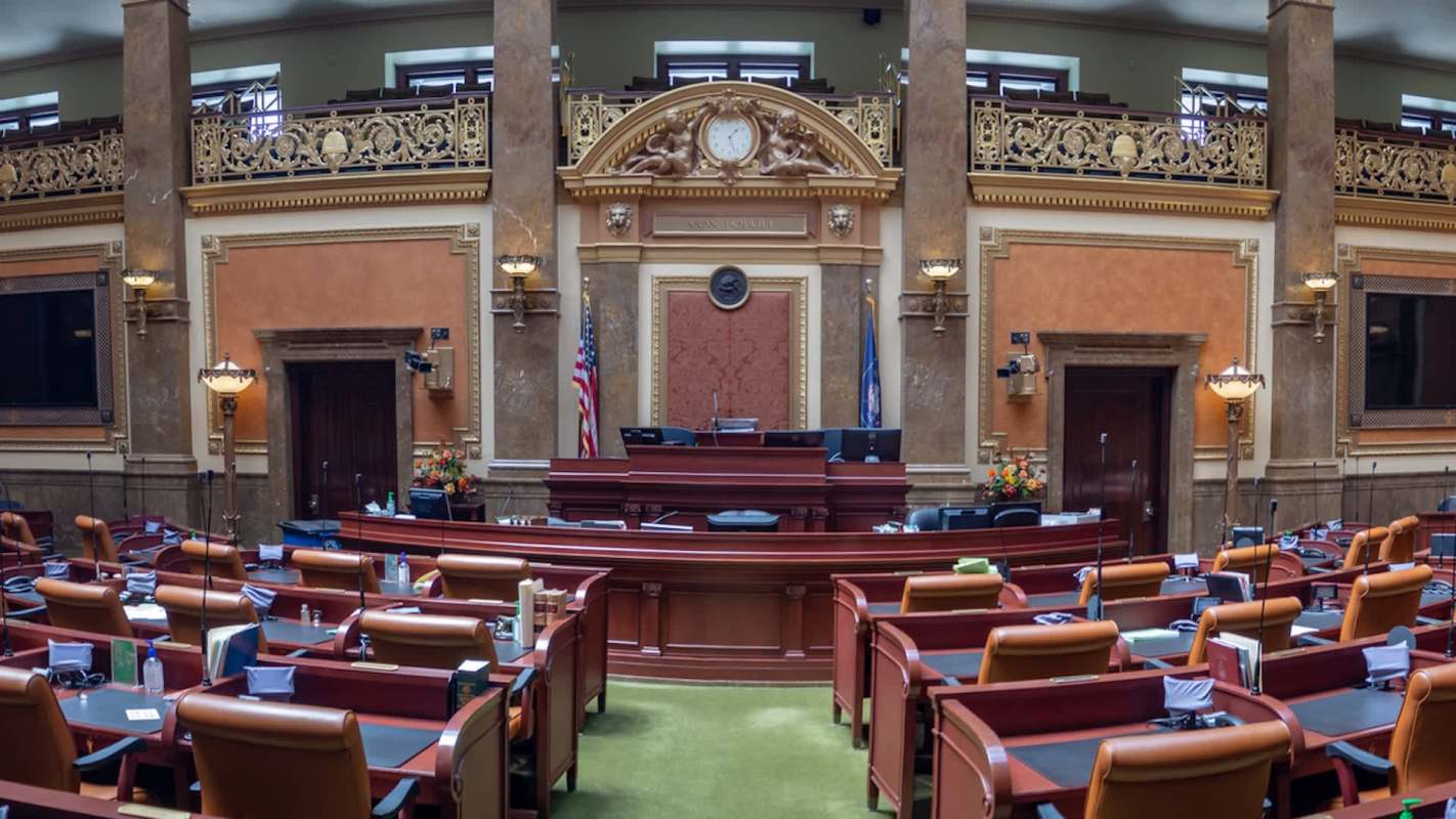 A large legislative chamber featuring ornate decor, chairs arranged for seating, and a prominent speaker's podium.
