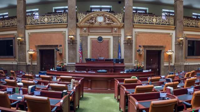 A large legislative chamber featuring ornate decor, chairs arranged for seating, and a prominent speaker's podium.