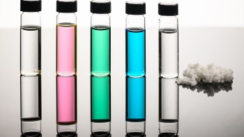 Five vials containing colorful liquids and a pile of salt on a reflective surface.