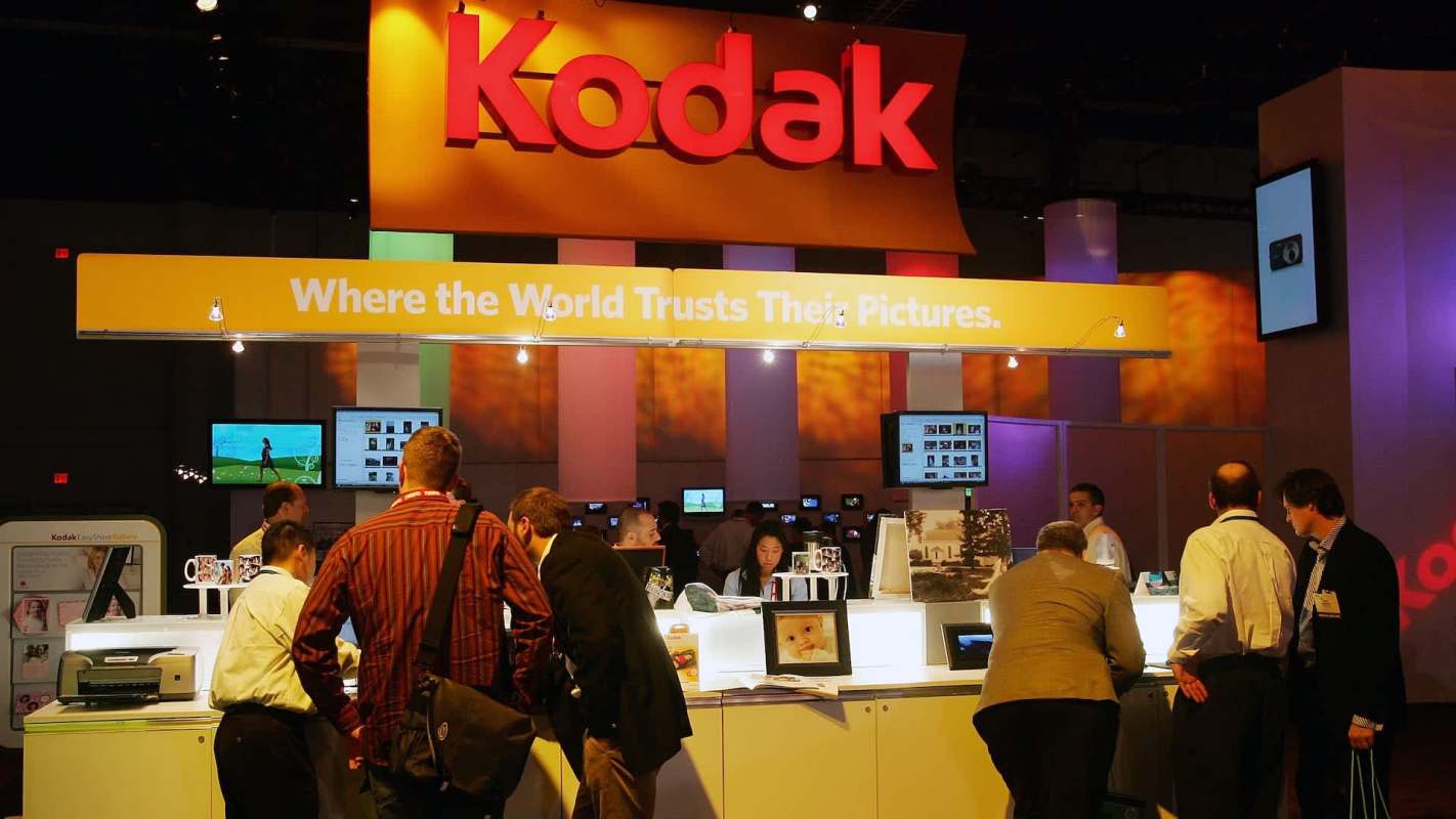 A bustling Kodak booth at a trade show, featuring displays and visitors interacting with photo equipment.