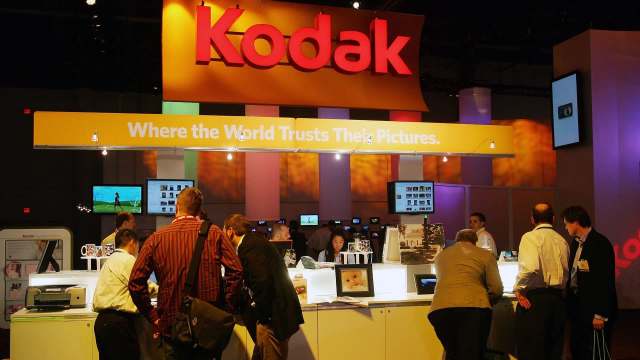 A bustling Kodak booth at a trade show, featuring displays and visitors interacting with photo equipment.