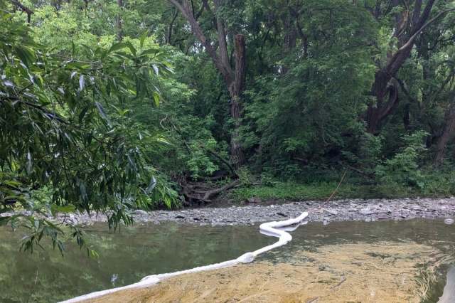 A white absorbent barrier is placed along a creek surrounded by lush green foliage and trees.