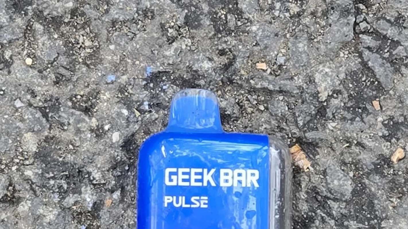 A blue disposable vape pen labeled "GEEK BAR PULSE" lying on a textured asphalt surface.
