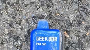 A blue disposable vape pen labeled "GEEK BAR PULSE" lying on a textured asphalt surface.