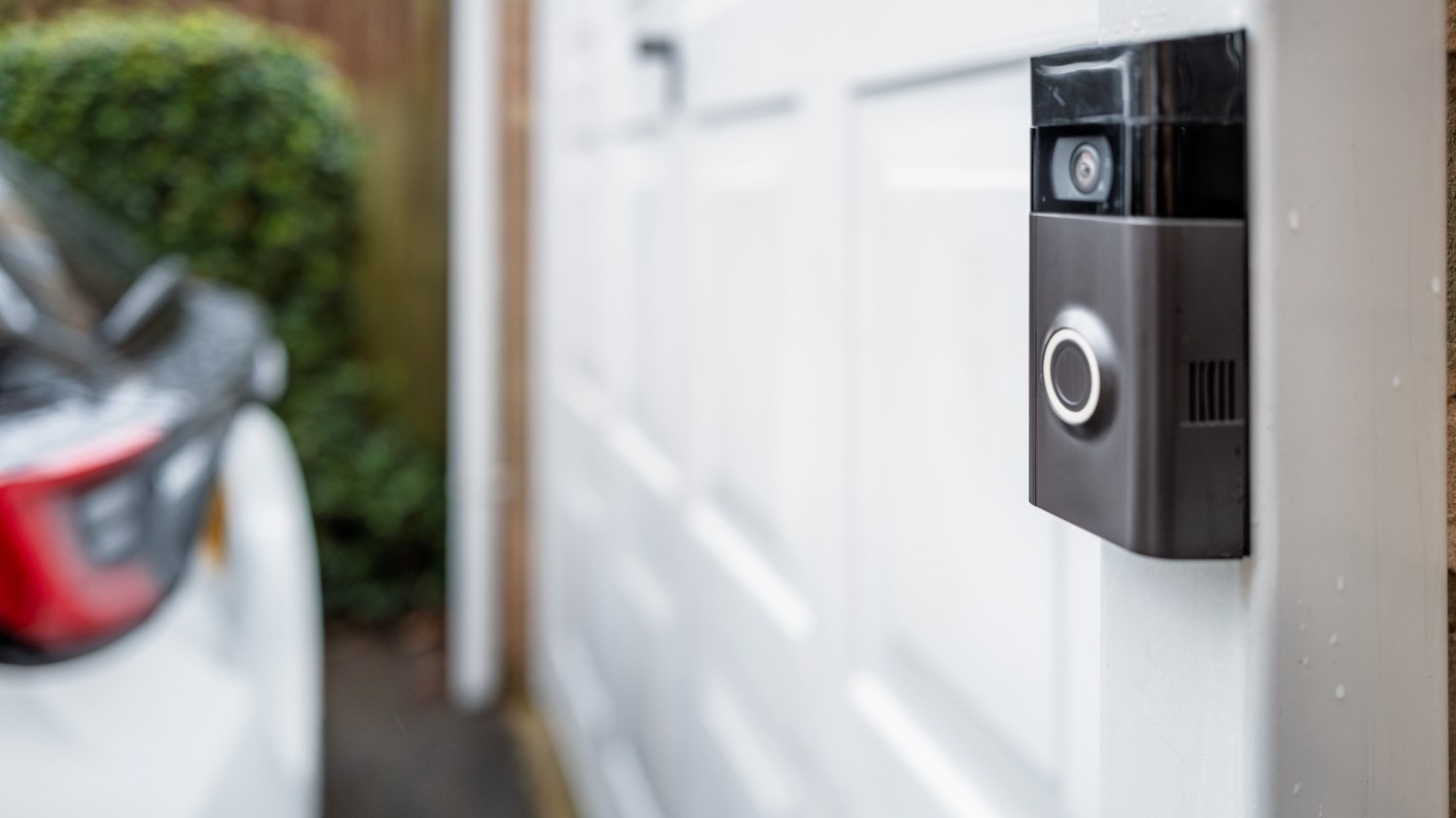 A close-up of a video doorbell mounted on a white garage door with a blurred car in the background.
