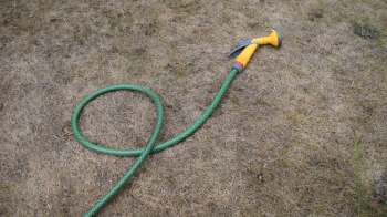 A green garden hose lies on dry, brown grass, with a yellow spray nozzle attached.