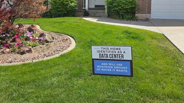 A humorous sign in a yard stating, "This home identifies as a data center and will use whatever amount of water it wants."