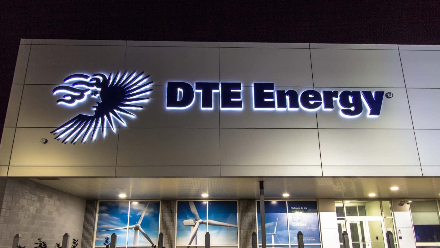 A well-lit DTE Energy sign with a stylized face logo is displayed on a modern building exterior at night.