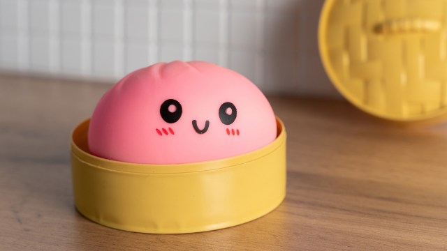 A cute pink dumpling squishy toy with a smiley face in a yellow steaming basket.
