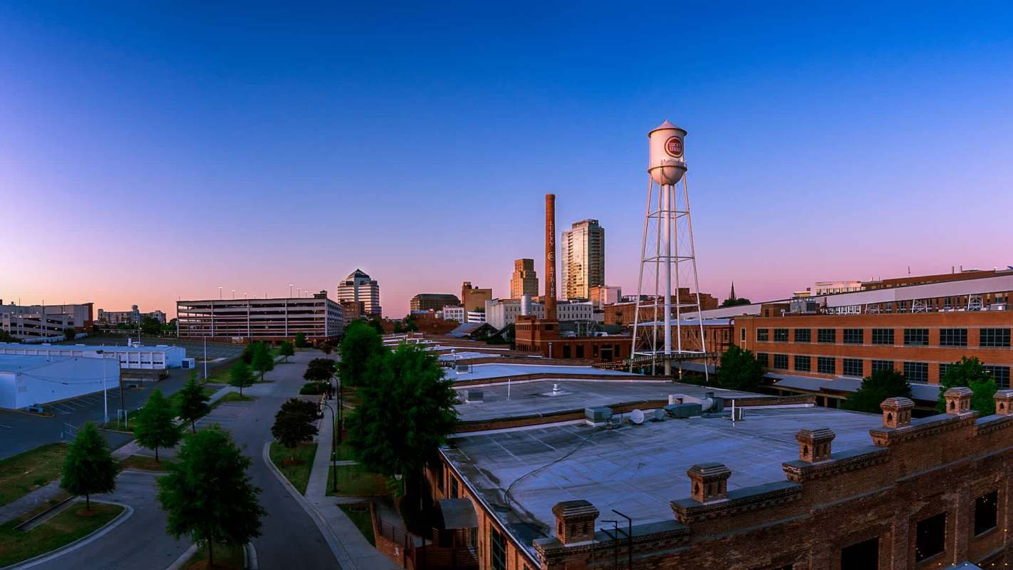 A city skyline at dusk featuring buildings, a water tower, and tree-lined streets.