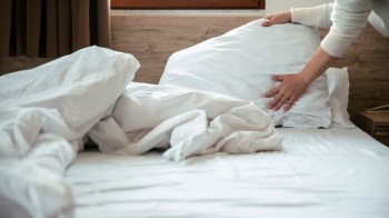 A person arranging white pillows on a neatly made bed with crumpled sheets.