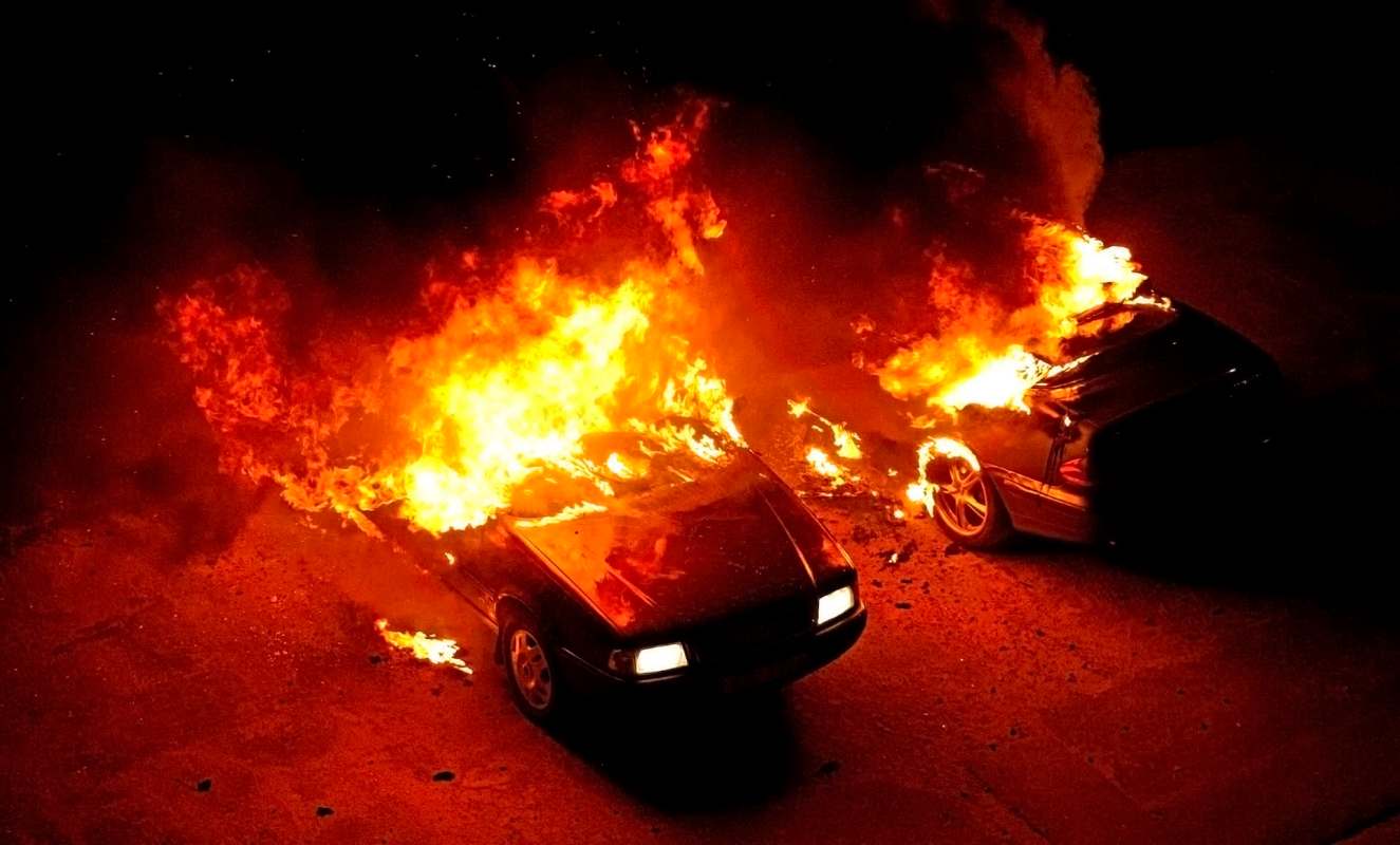 Two cars engulfed in flames at night.
