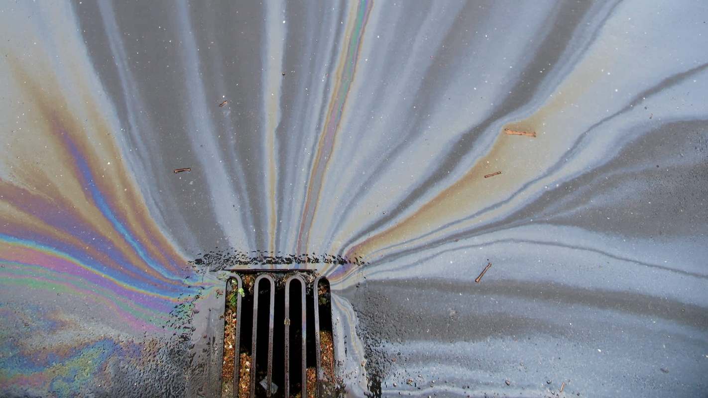Oil spilling from pavement into a storm drain.