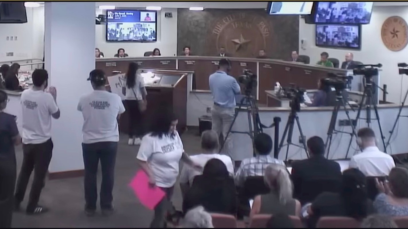 A public meeting featuring speakers and attendees, with cameras capturing the event.