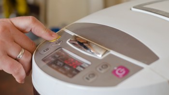 A hand pressing a yellow button on a multi-function kitchen appliance display.