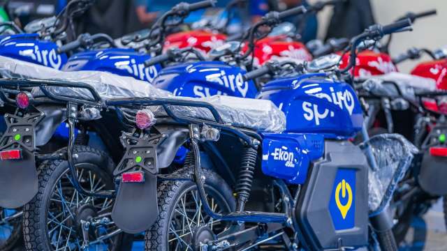 A row of newly manufactured blue and red motorcycles with the Spiro logo with protective coverings in a showroom.