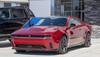 A bright red sports car parked in front of a dealership, alongside a black truck.