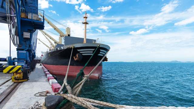 A cargo ship docked at a port with cranes and a clear blue sky in the background.