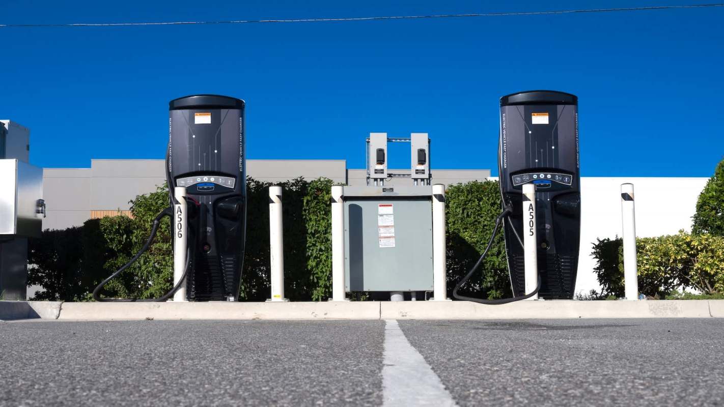 Two electric vehicle charging stations in front of green bushes.