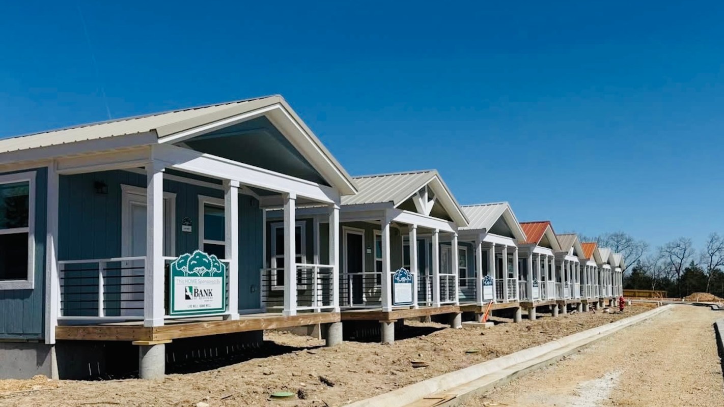 A row of newly constructed houses with porches and colorful roofs against a clear blue sky.