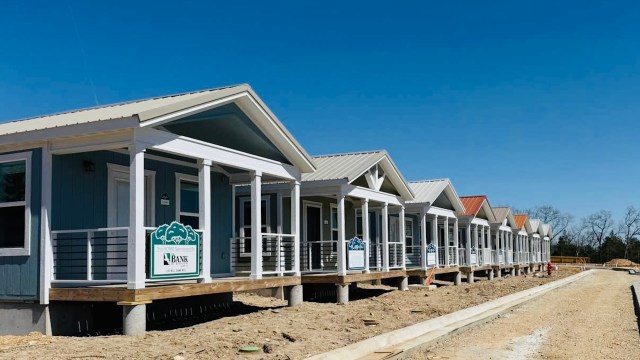 A row of newly constructed houses with porches and colorful roofs against a clear blue sky.