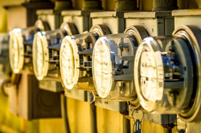A close-up of multiple electric meters mounted on a wall, displaying dials and wires.