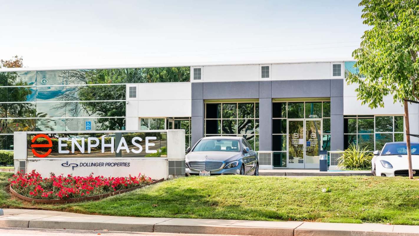 A modern office building with a prominent "Enphase" sign and parked cars, surrounded by landscaped greenery.