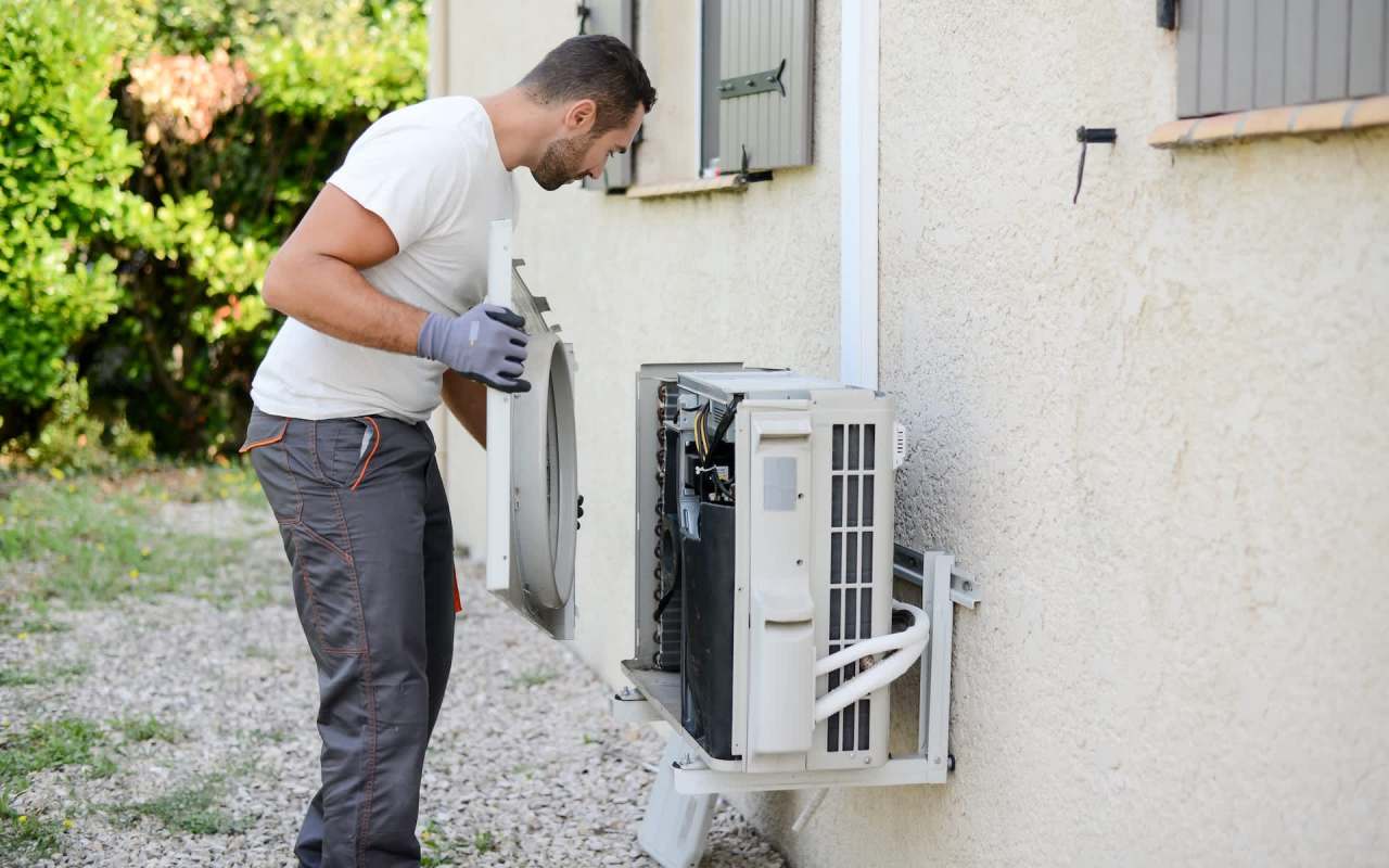 A technician inspects an outdoor heat pump unit while wearing gloves.