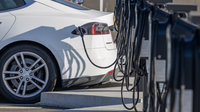 A white electric vehicle is charging at a station with cables in the foreground.