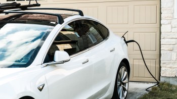 A white electric car is plugged into a charging station next to a garage door.